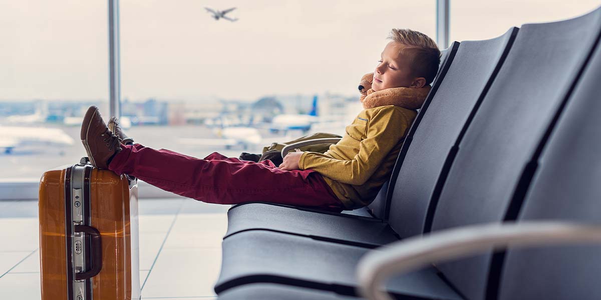 Kid flying alone during the holidays, sitting relaxed in airport with suitcase.