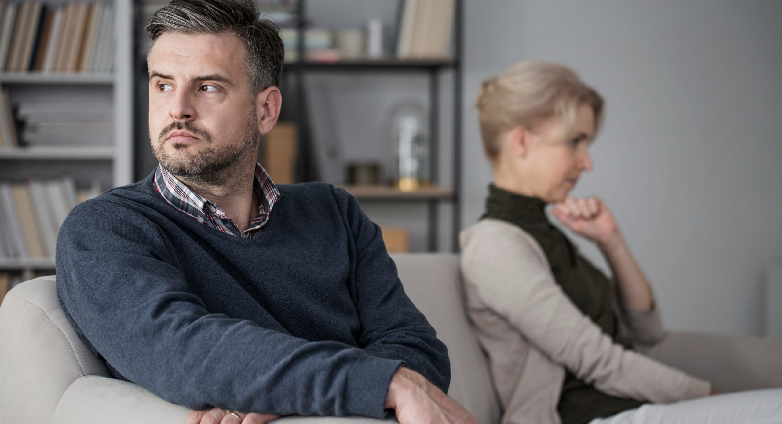 Couple sitting separately on couch, contemplating signs of divorce